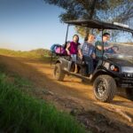 Family riding golf cart in dirt road.