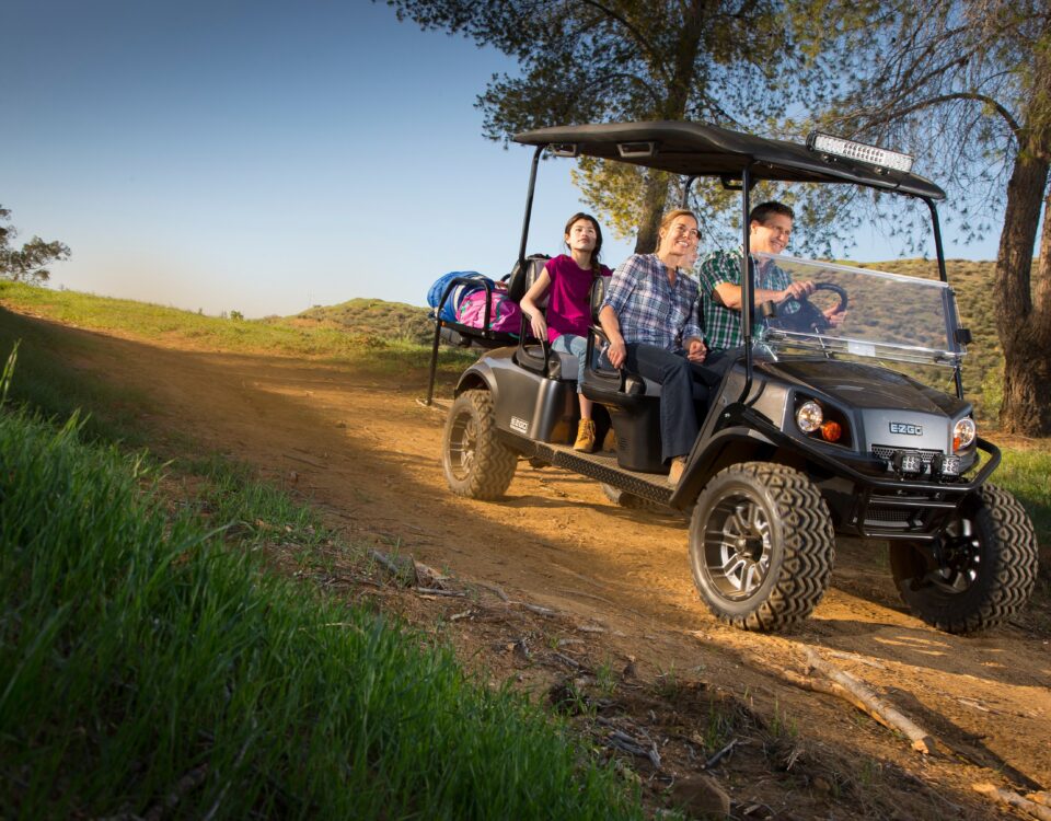 Family riding golf cart in dirt road.