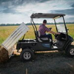 Man riding golf cart in field dumping hay.