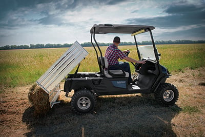 Man riding golf cart in field dumping hay.