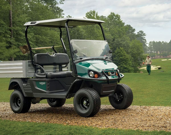 Green Cushman golf cart used for lawn care and parked on golf course.