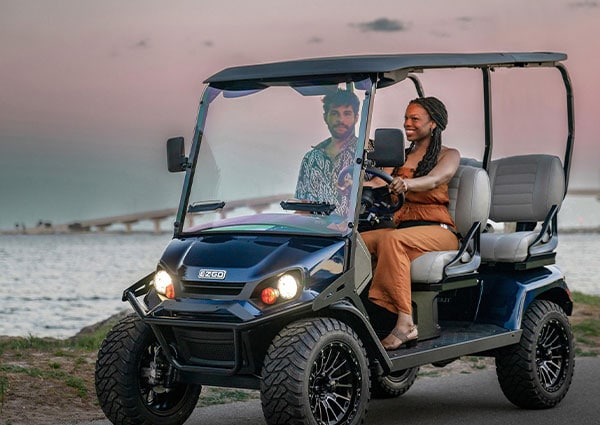Couple riding E-ZGO golf cart at beach.