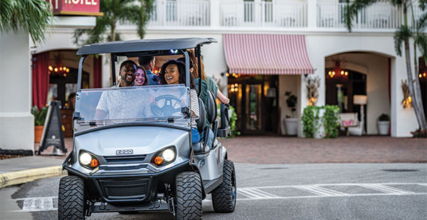 Friends driving golf cart by shops.