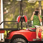 Boy taking a photo while sitting inside red golf cart.