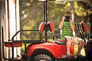 Boy taking a photo while sitting inside red golf cart.