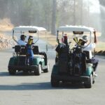 Two men riding golf cart along course.