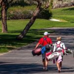 Father and son carrying golf equipment and walking.