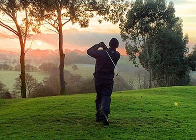Man golfing with sunset in the back.